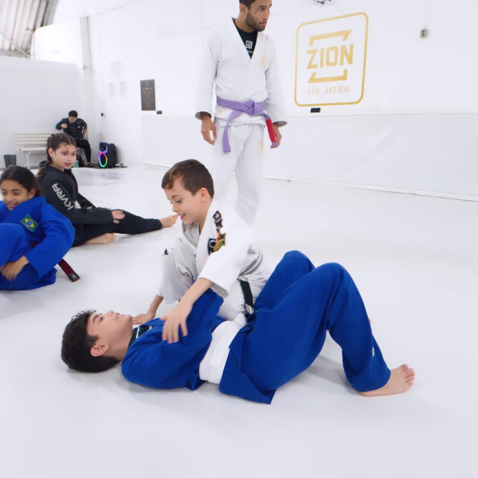 Aula infantil na Zion Jiu-Jitsu com professor acompanhando o treino